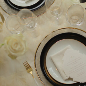 Bestek met witte handvatten en goud huren Wit-gouden bestek naast zwart-wit servies, glaswerk en witte rozen