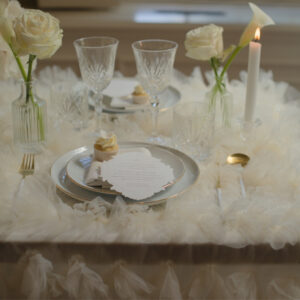 Wit-gouden bestek voor een feestelijk diner Gedekte tafel met wit-gouden bestek, glazen onderborden, glaswerk en witte bloemen