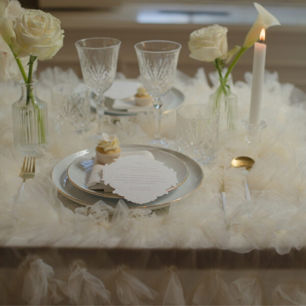 Wit-gouden bestek voor een feestelijk diner Gedekte tafel met wit-gouden bestek, glazen onderborden, glaswerk en witte bloemen