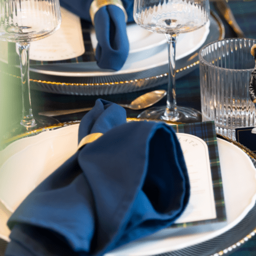 Navy blauwe servet gevouwen op bord met goud bestek bij stijlvolle bruiloft tafelstyling