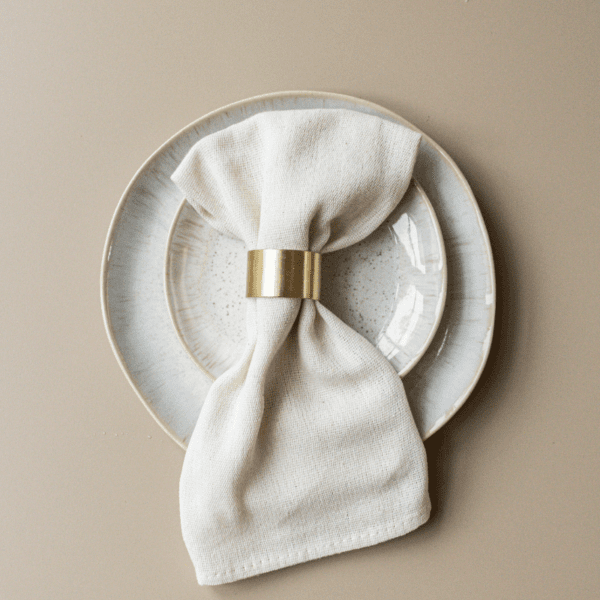 servet ring goud voor bruiloft Gouden servetring met wit servet op bord – stijlvolle tafeldecoratie voor bruiloft of diner