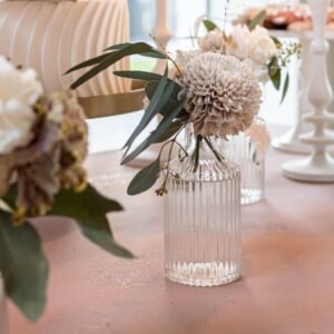 Glazen ribbelvaasje huren Glazen ribbelvaasje met lichte bloemen en groene takken op een roze tafel tijdens sweet sixteen feestje