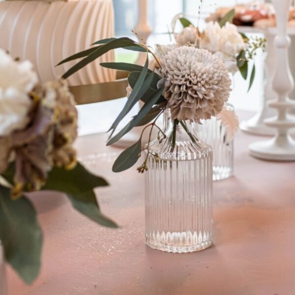 Glazen ribbelvaasje huren Glazen ribbelvaasje met lichte bloemen en groene takken op een roze tafel tijdens sweet sixteen feestje