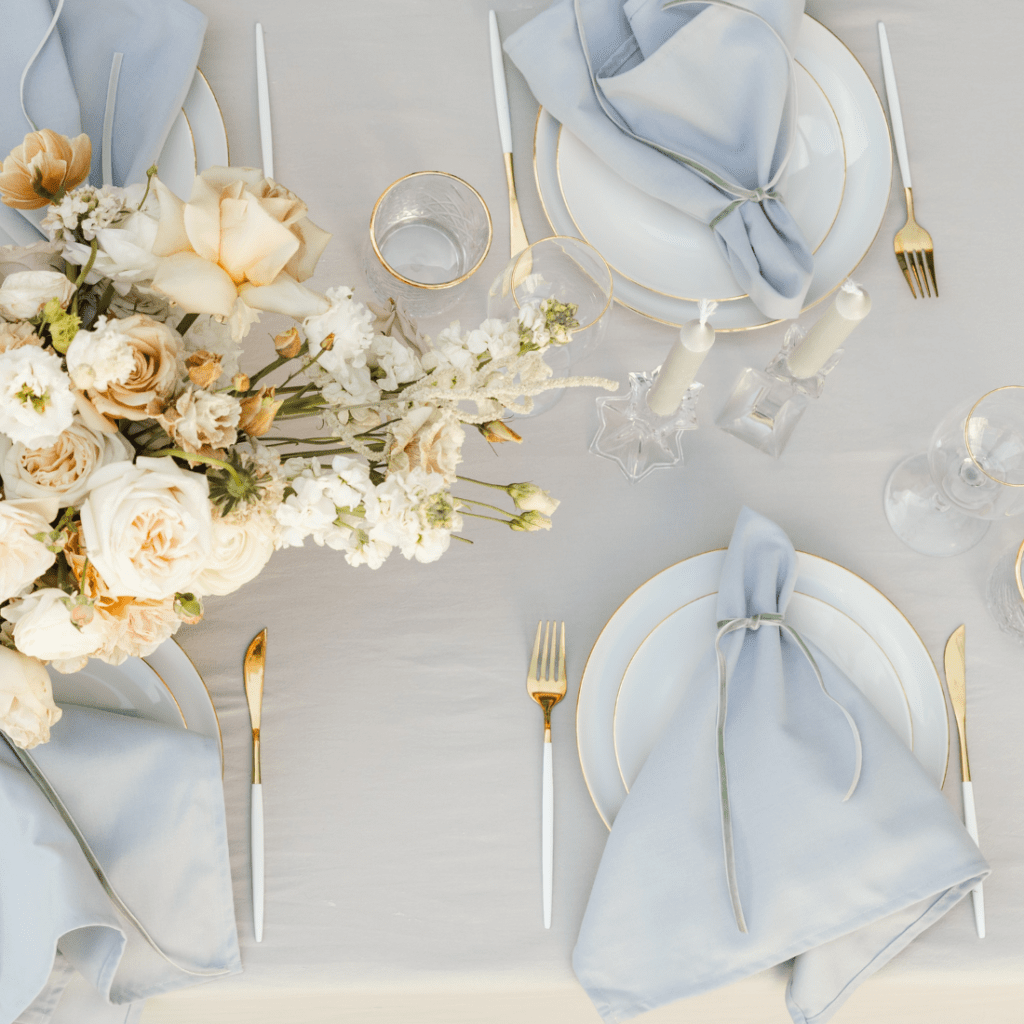 Stijlvolle bruilofttafel met lichtblauwe servetten, gouden bestek en wit servies – styling bruiloft tips