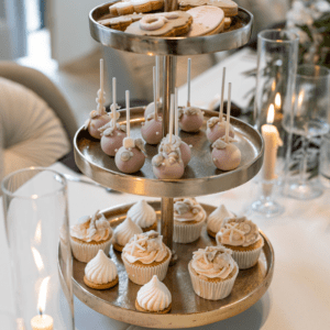 Gouden etagère met 3 lagen met cupcakes en gebak op stijlvolle bruiloftstafel met bloemen en kaarsen