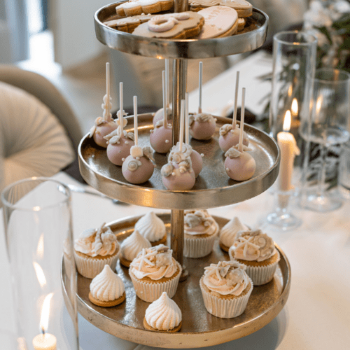 Gouden etagère met 3 lagen met cupcakes en gebak op stijlvolle bruiloftstafel met bloemen en kaarsen