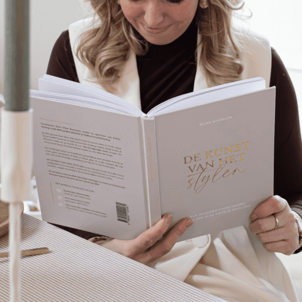 Sfeer begint bij kiezen Vrouw leest het stylingboek De kunst van het stylen aan een gedekte tafel, als basis voor het creëren van sfeer tijdens een bruiloft.