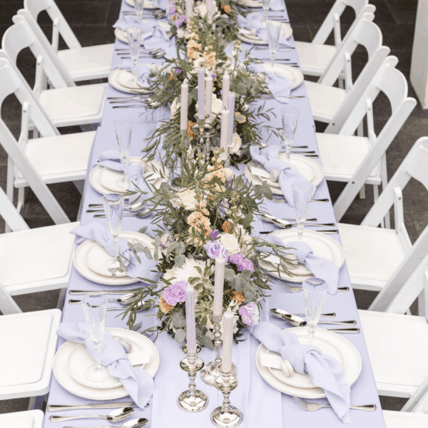 Zilverlook bestek in elegante tafeldecoratie met paarse accenten Zilverlook bestek gecombineerd met lila tafelloper en pastelkleurige bloemen.