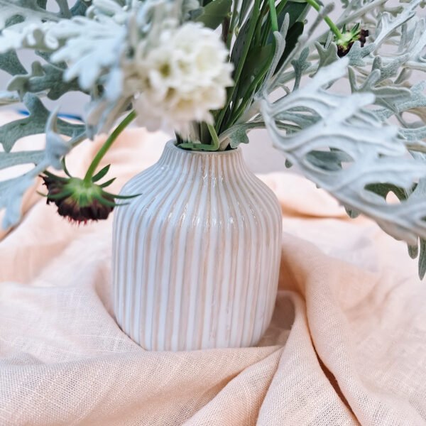 Beige ribbelvaasje met bloemstuk – stijlvolle tafeldecoratie Beige ribbelvaasje met bloemenarrangement in zachte tinten, ideaal voor bruiloft styling.