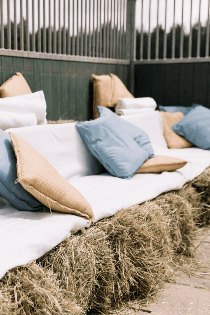 Buitenstyling met hooibalen en verhuurbare blauwe kussens – informele loungehoek bij bruiloft