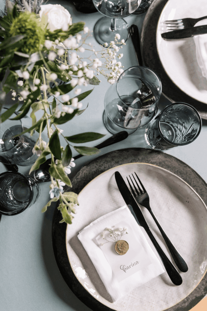 Trouwtafel met zachte kleuren, zwart bestek en natuurlijke accenten zoals groen en waxstempel – voorbeeld van verfijnde styling