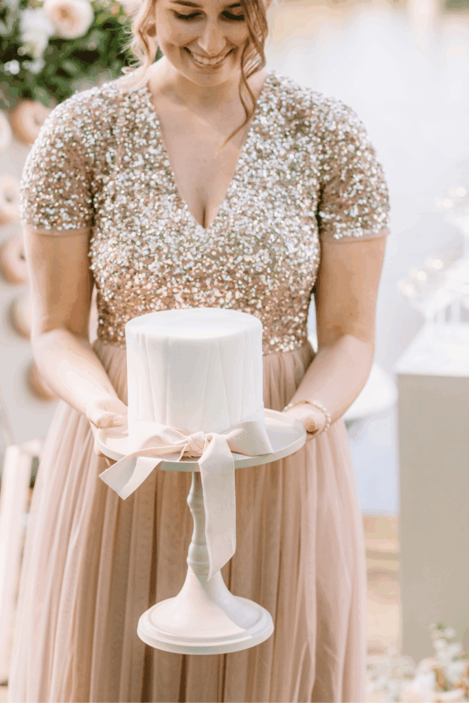 Bruid in glinsterende jurk snijdt witte bruidstaart tijdens stijlvolle bruiloft – voorbeeld van bewuste styling binnen trouwbudget