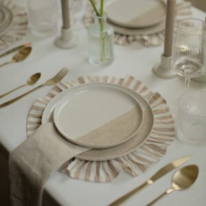 Champagnegoud bestek naast een wit-beige dinerbord op gestreept onderbord