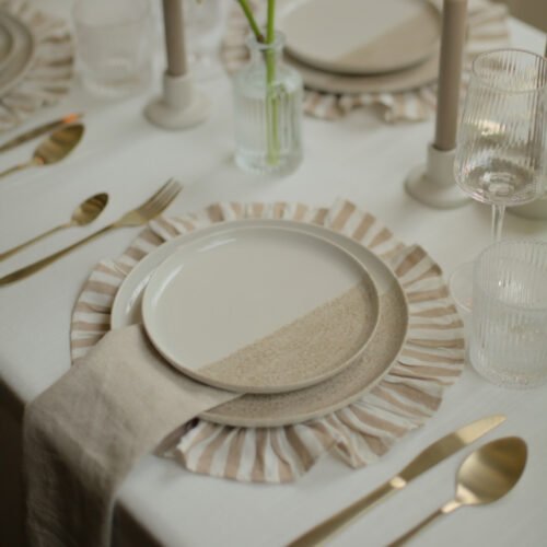 Champagnegoud bestek naast een wit-beige dinerbord op gestreept onderbord