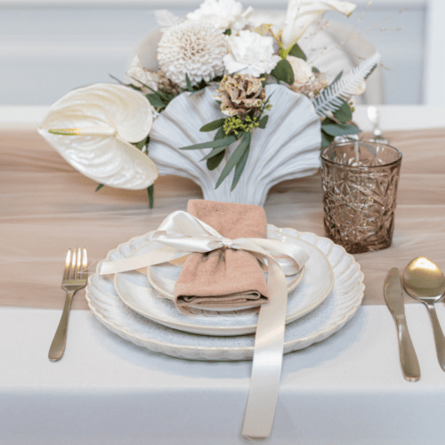 Gedekte bruiloft tafel met beige lunchbordje, linnen servet en goud bestek