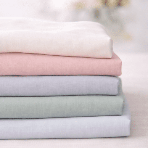 Luchtig katoen in ivoor soepel over een lange tafel gedrapeerd met lichte transparantie, gebruikt als tafelloper voor bruiloft styling in rustige neutrale tinten