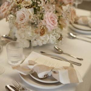 Tafeldecoratie met wit-beige gestreepte servetten Gedekte tafel met wit-beige gestreepte servetten, glaswerk en een bloemstuk in wit en zachtroze.