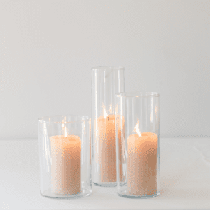 Drie glazen cilinder windlichten met zachte kaarsen in warme neutrale tinten op een rustige lichte ondergrond voor verhuur kaarsenstandaard bruiloft