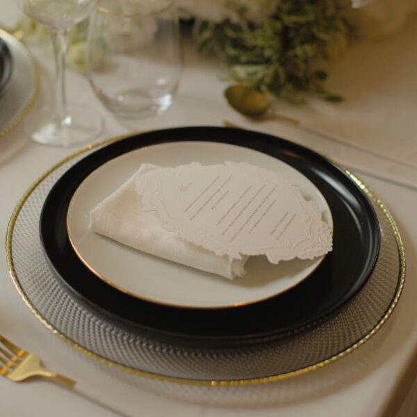 Glazen onderbord met zwart-wit servies Glazen onderbord met gouden rand onder gestapeld servies in een elegante en klassieke tafelsetting in zwart wit