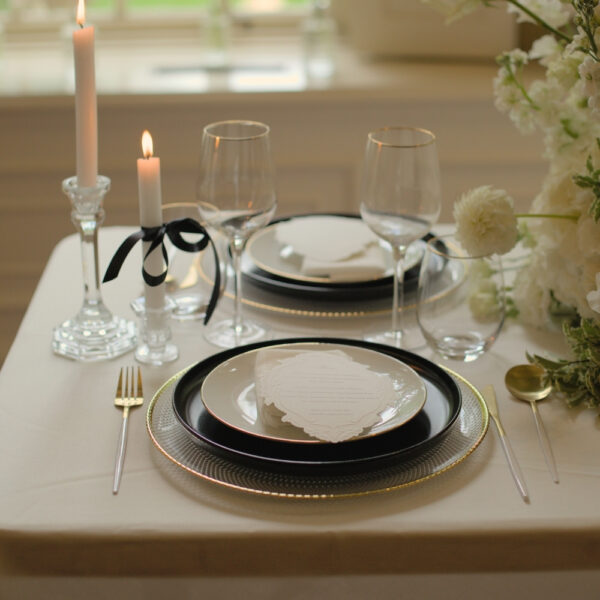 Onderborden met gouden rand voor een bruiloft Glazen onderborden met champagnegouden rand op een tafel met zwart-wit servies en kaarslicht