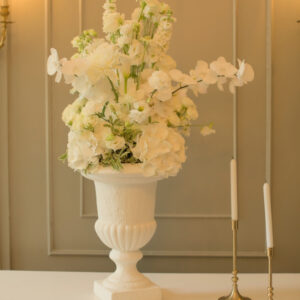 Witte vaas met witte bloemen en groen Klassieke witte vaas met een brede rand, gevuld met witte bloemen en groene takken. Te huur bij Feline Styling