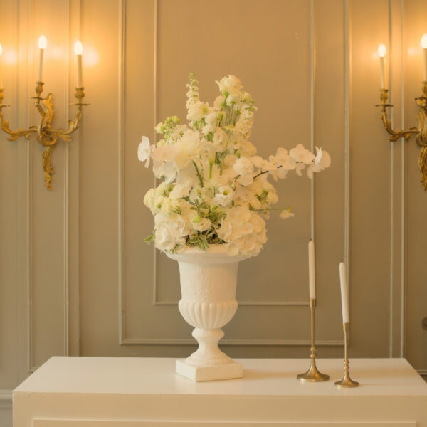 Klassieke witte vaas met luchtig bloemstuk Witte vaas met een luchtig bloemstuk van lichte bloemen en groene takken bij kaarslicht.