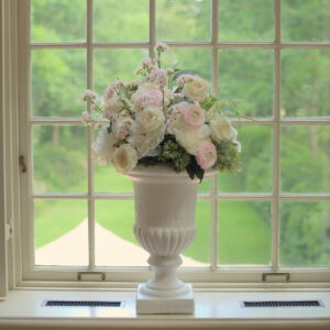 Klassieke witte vaas op een vensterbank, gevuld met witte en zachtroze bloemen. Grote witte vaas op voet met roze en witte bloemen