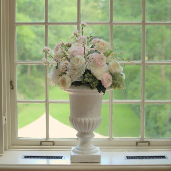 Klassieke witte vaas op een vensterbank, gevuld met witte en zachtroze bloemen. Grote witte vaas op voet met roze en witte bloemen
