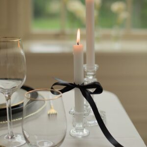 Waterglas met gouden rand naast dinerkaarsen en zwart lint
