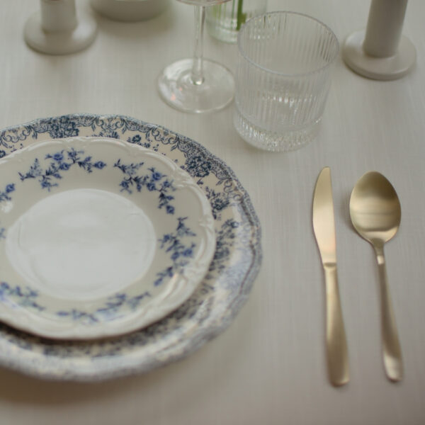 Blauw-wit servies huren voor een 21 diner Bord met blauwe bloemen en wit servet naast goudkleurig bestek en glaswerk