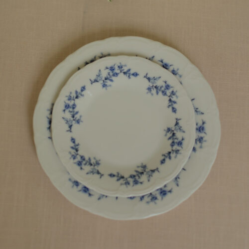 Wit ontbijt- en lunchbord met blauwe bloemen en golvende rand op een beige tafelkleed